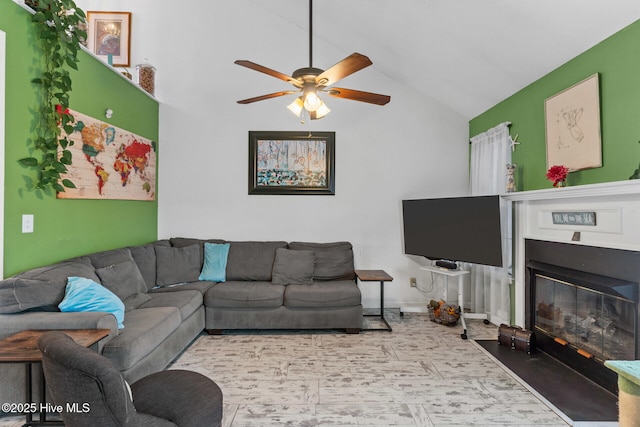 living area with vaulted ceiling, a fireplace with flush hearth, and a ceiling fan