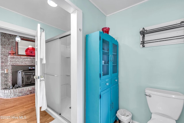 bathroom with a shower stall, toilet, a wood stove, and wood finished floors