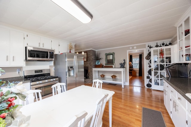 kitchen with light wood finished floors, ornamental molding, appliances with stainless steel finishes, a fireplace, and white cabinets