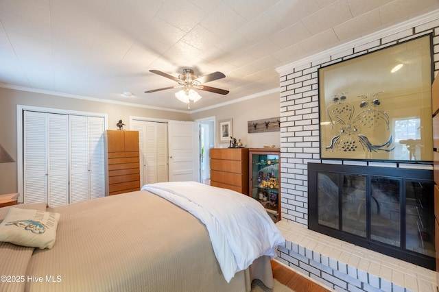 bedroom featuring a ceiling fan, crown molding, a fireplace, and multiple closets