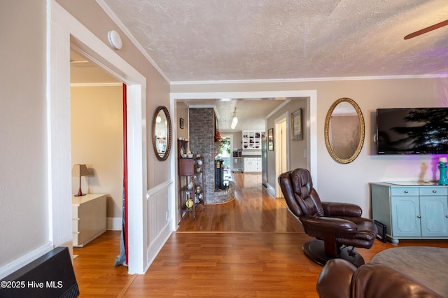 living area featuring crown molding, wood finished floors, baseboards, and a textured ceiling