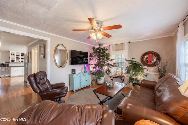 living area with ceiling fan, a textured ceiling, wood finished floors, and crown molding