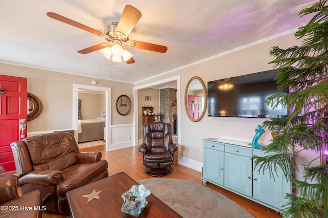 living room featuring a ceiling fan, wood finished floors, baseboards, a textured ceiling, and crown molding