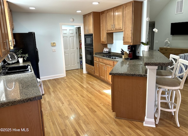 kitchen featuring visible vents, a breakfast bar, a peninsula, black appliances, and a sink