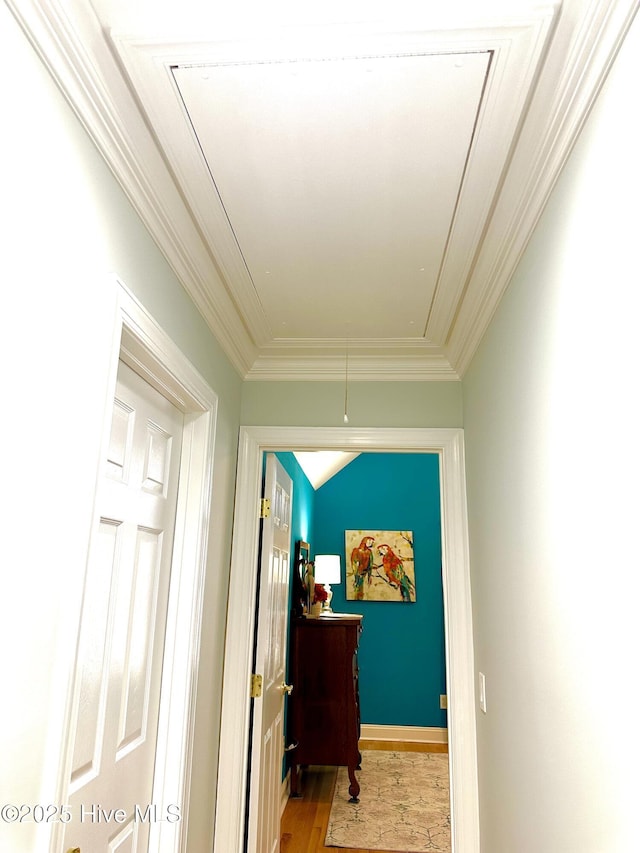 hall with attic access, light wood-style floors, ornamental molding, and baseboards