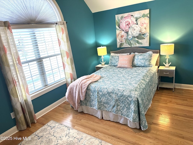 bedroom with vaulted ceiling, baseboards, and wood finished floors