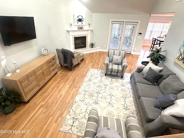 living room featuring light wood-style floors, lofted ceiling, a glass covered fireplace, and baseboards