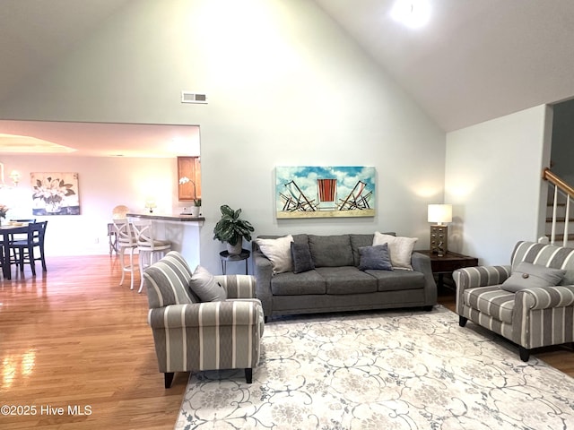 living area featuring light wood-type flooring, high vaulted ceiling, stairs, and visible vents