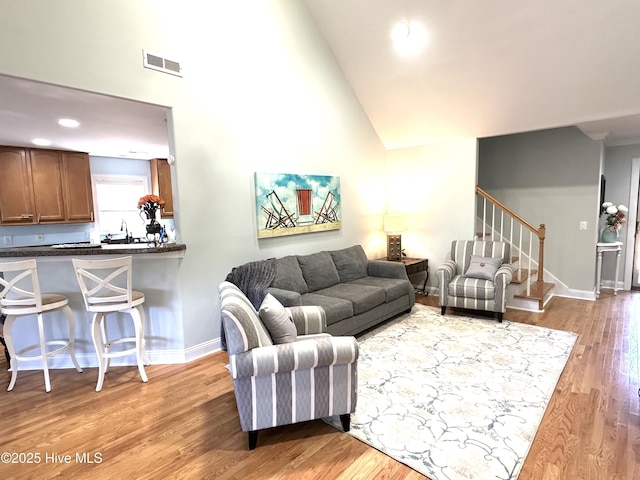 living room featuring baseboards, visible vents, stairs, light wood-type flooring, and high vaulted ceiling