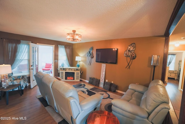 living room with baseboards, wood finished floors, a textured ceiling, french doors, and a fireplace