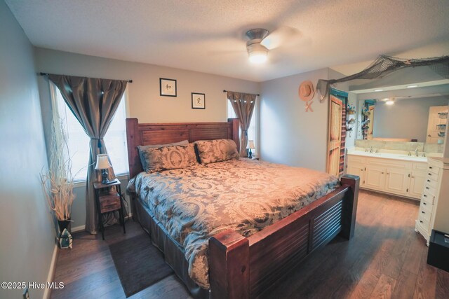 bedroom featuring dark wood finished floors, ensuite bathroom, a sink, a textured ceiling, and baseboards