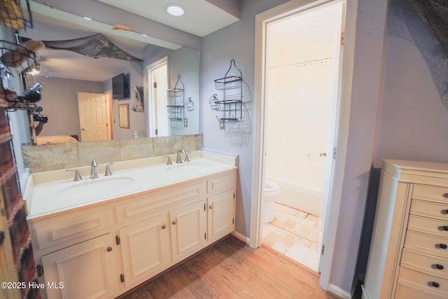 full bathroom with double vanity, wood finished floors, a sink, and toilet