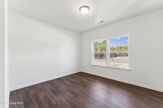 spare room featuring visible vents, dark wood finished floors, and baseboards