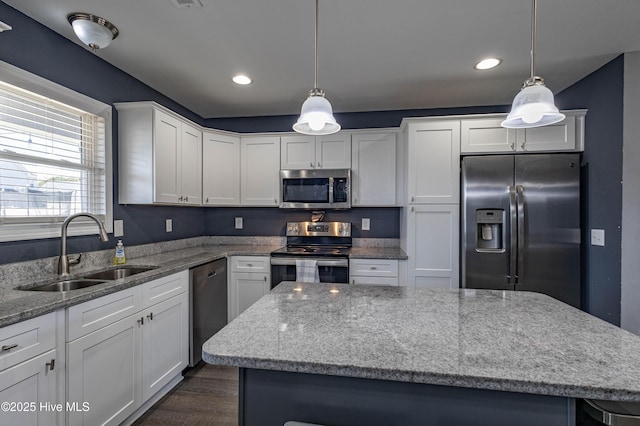 kitchen with a center island, appliances with stainless steel finishes, white cabinets, a sink, and light stone countertops