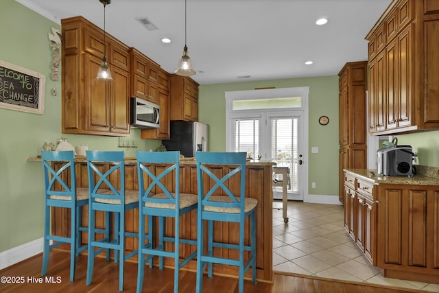 kitchen featuring brown cabinetry, visible vents, a peninsula, appliances with stainless steel finishes, and a kitchen bar