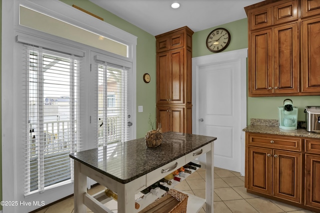 kitchen with dark stone countertops, light tile patterned floors, and brown cabinets