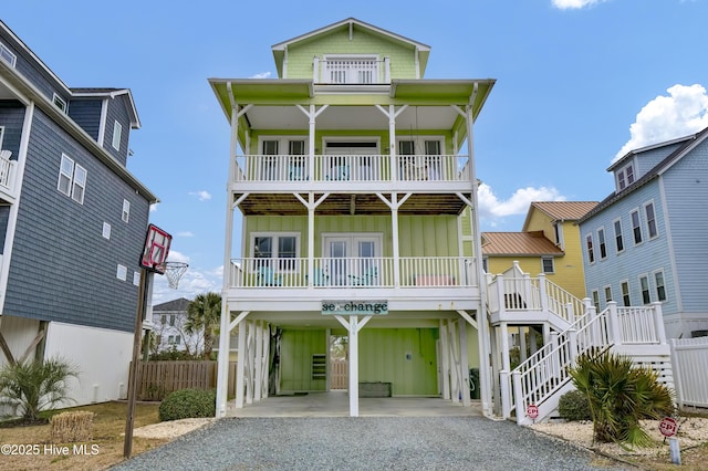 raised beach house with a porch, a balcony, gravel driveway, board and batten siding, and a carport