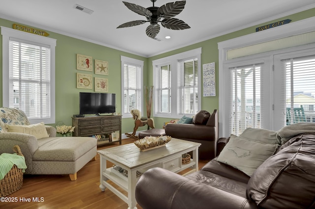 living area featuring visible vents, wood finished floors, a healthy amount of sunlight, and ornamental molding