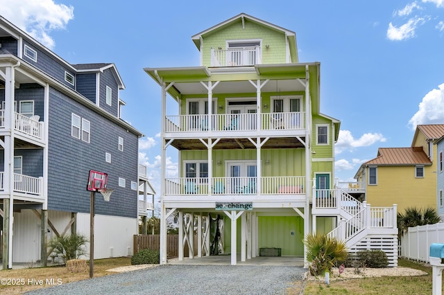 coastal home featuring board and batten siding, gravel driveway, stairway, a balcony, and a carport