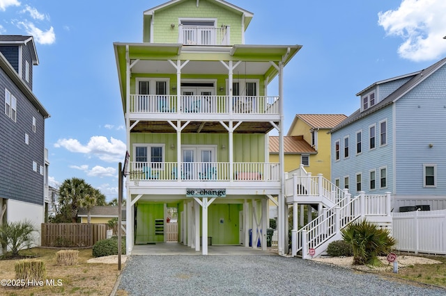 coastal home with a porch, a balcony, gravel driveway, board and batten siding, and a carport