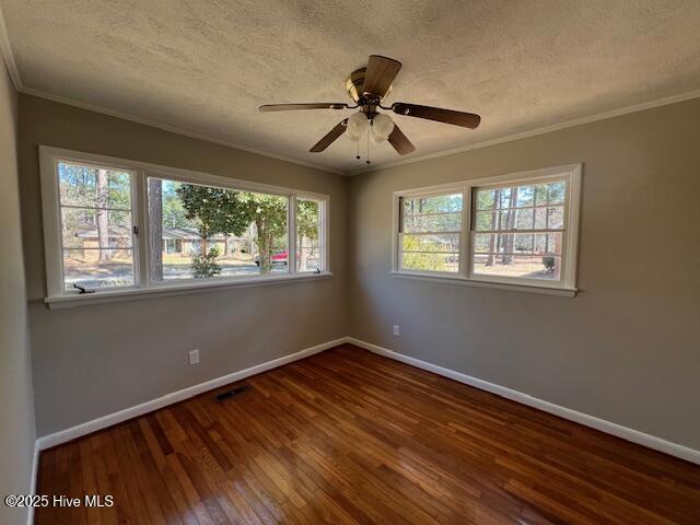 spare room with ornamental molding, visible vents, baseboards, and wood finished floors