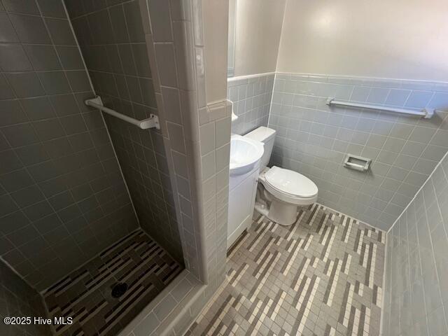 full bath with tile patterned flooring, toilet, a wainscoted wall, tile walls, and a stall shower