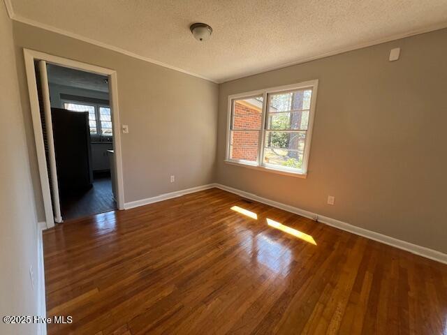 spare room featuring crown molding, dark wood finished floors, a textured ceiling, and baseboards