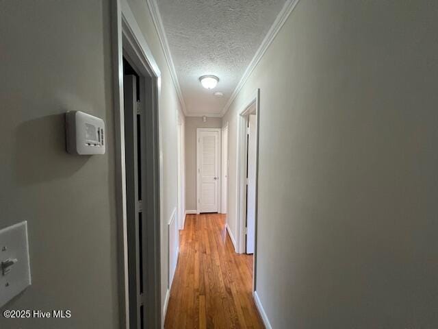 hallway with crown molding, baseboards, a textured ceiling, and wood finished floors