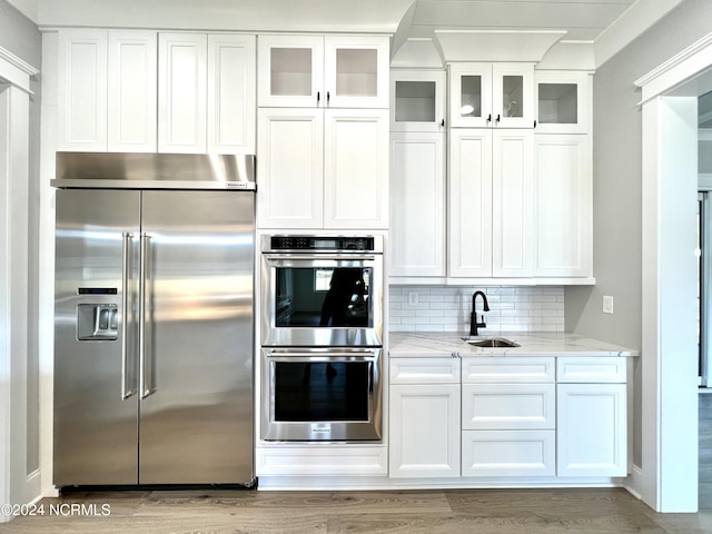 kitchen featuring appliances with stainless steel finishes, light stone counters, light wood-type flooring, white cabinetry, and a sink