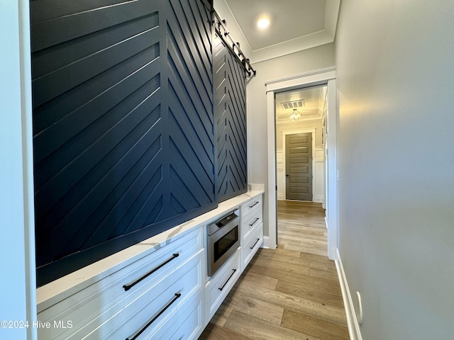 hall with crown molding, visible vents, light wood-style flooring, a barn door, and baseboards