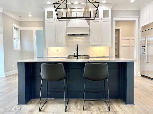 kitchen with an island with sink, custom exhaust hood, ornamental molding, and built in fridge