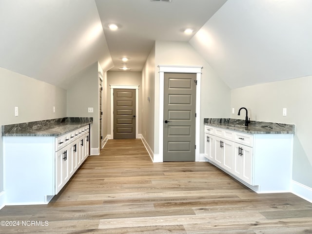 kitchen with vaulted ceiling, light wood-style flooring, a sink, and white cabinetry