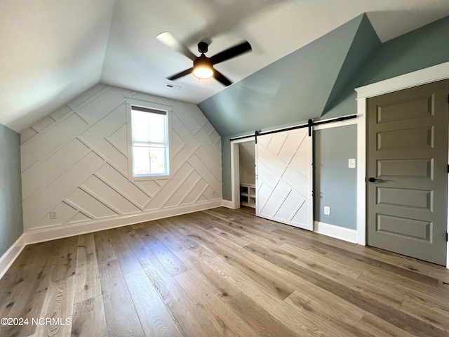 bonus room featuring ceiling fan, a barn door, wood finished floors, visible vents, and vaulted ceiling