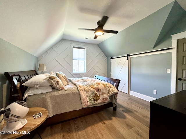 bedroom featuring a ceiling fan, lofted ceiling, wood finished floors, and a barn door