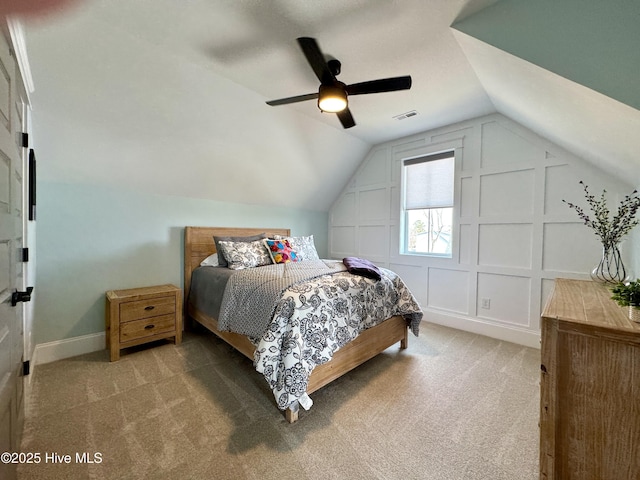 carpeted bedroom with a decorative wall, a ceiling fan, baseboards, vaulted ceiling, and visible vents