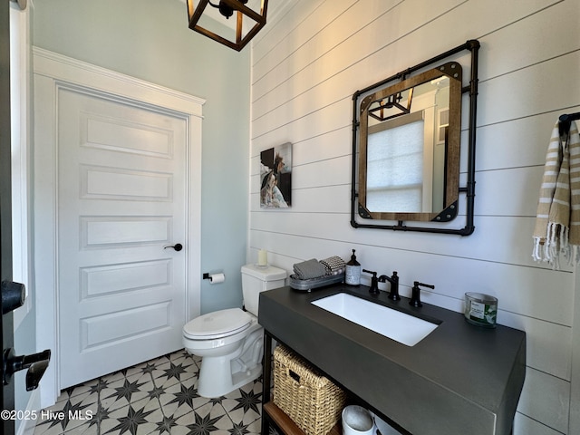 bathroom with toilet, wooden walls, vanity, and tile patterned floors