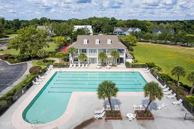 community pool with a patio area, fence, and a lawn