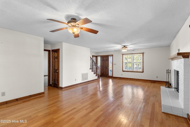 unfurnished living room with a textured ceiling, light wood-style flooring, visible vents, stairway, and a brick fireplace