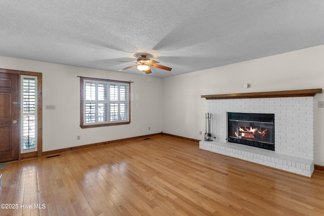 unfurnished living room with a textured ceiling, visible vents, baseboards, light wood-style floors, and a brick fireplace