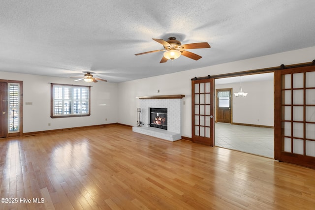 unfurnished living room with light wood finished floors, a barn door, a fireplace, and a ceiling fan