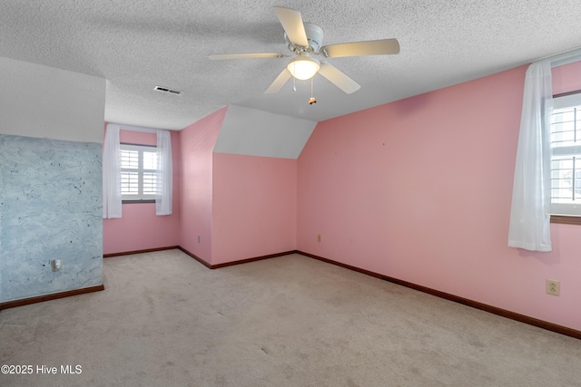 additional living space with visible vents, baseboards, carpet, vaulted ceiling, and a textured ceiling