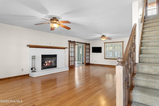 unfurnished living room with a barn door, baseboards, a ceiling fan, stairs, and light wood-style floors