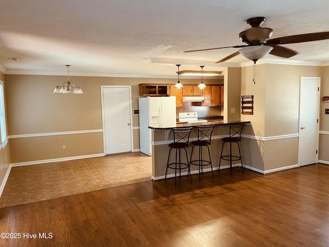 kitchen with under cabinet range hood, a peninsula, white appliances, brown cabinetry, and dark wood finished floors