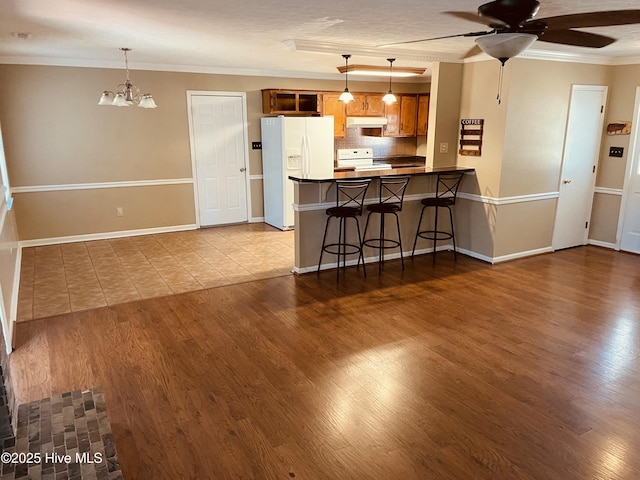 kitchen featuring brown cabinets, crown molding, backsplash, white appliances, and under cabinet range hood