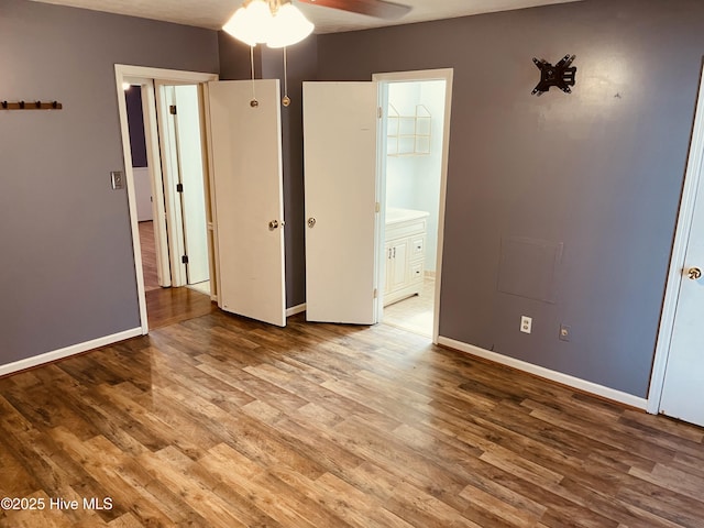 unfurnished bedroom featuring baseboards, wood finished floors, and ensuite bathroom