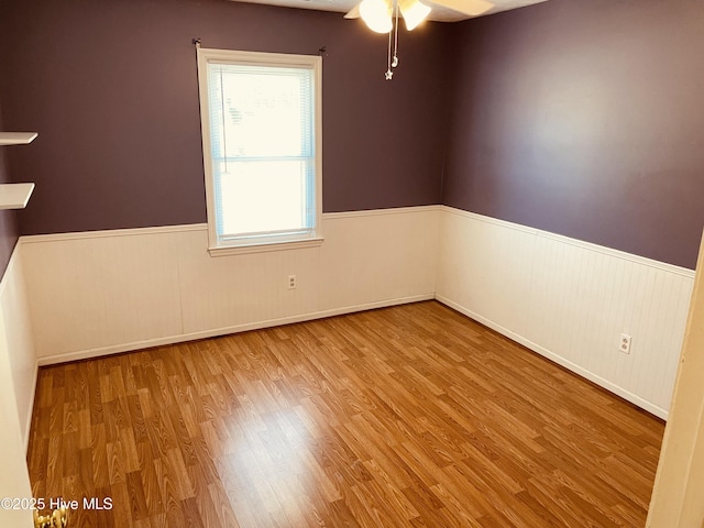 spare room featuring a ceiling fan, wainscoting, and wood finished floors