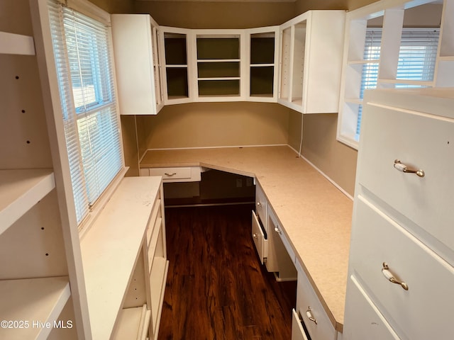 kitchen with light stone counters, white cabinetry, dark wood-style floors, built in desk, and glass insert cabinets