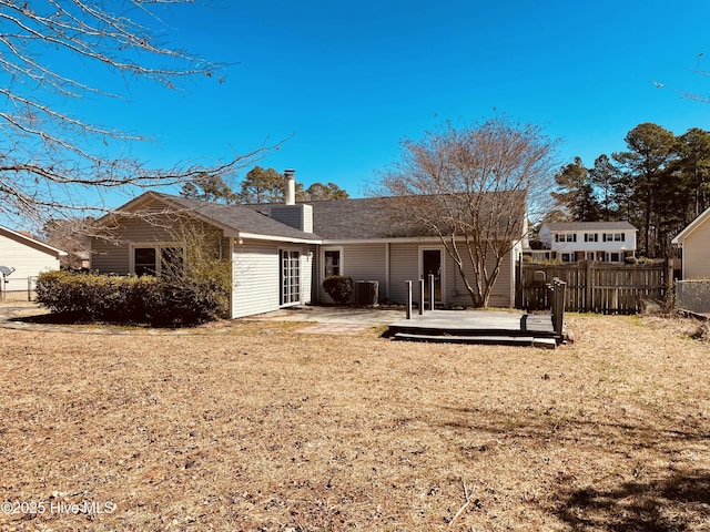 rear view of property with a deck, a yard, a chimney, and fence