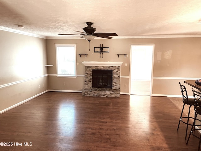 unfurnished living room with dark wood finished floors, ceiling fan, a textured ceiling, crown molding, and a brick fireplace