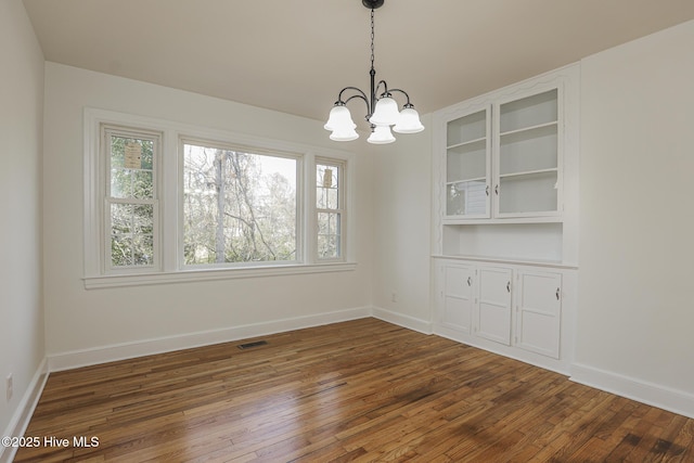 unfurnished dining area featuring visible vents, dark wood finished floors, baseboards, and an inviting chandelier